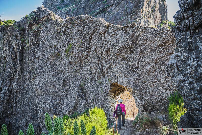 hiker walking under an arch carved in the mountain on pr1 pico arieiro hike