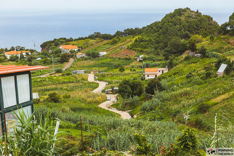a curvy zigzag path surrounded by farms and some houses, ocean seen in the background